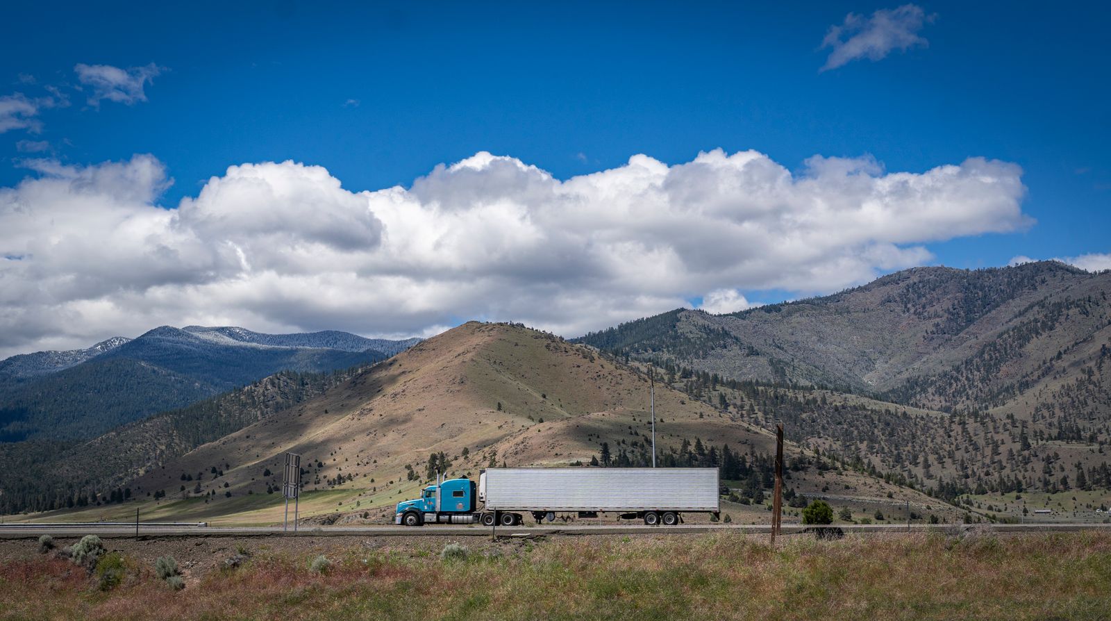 American semi truck driving on a US rural highway with mountains in the background.